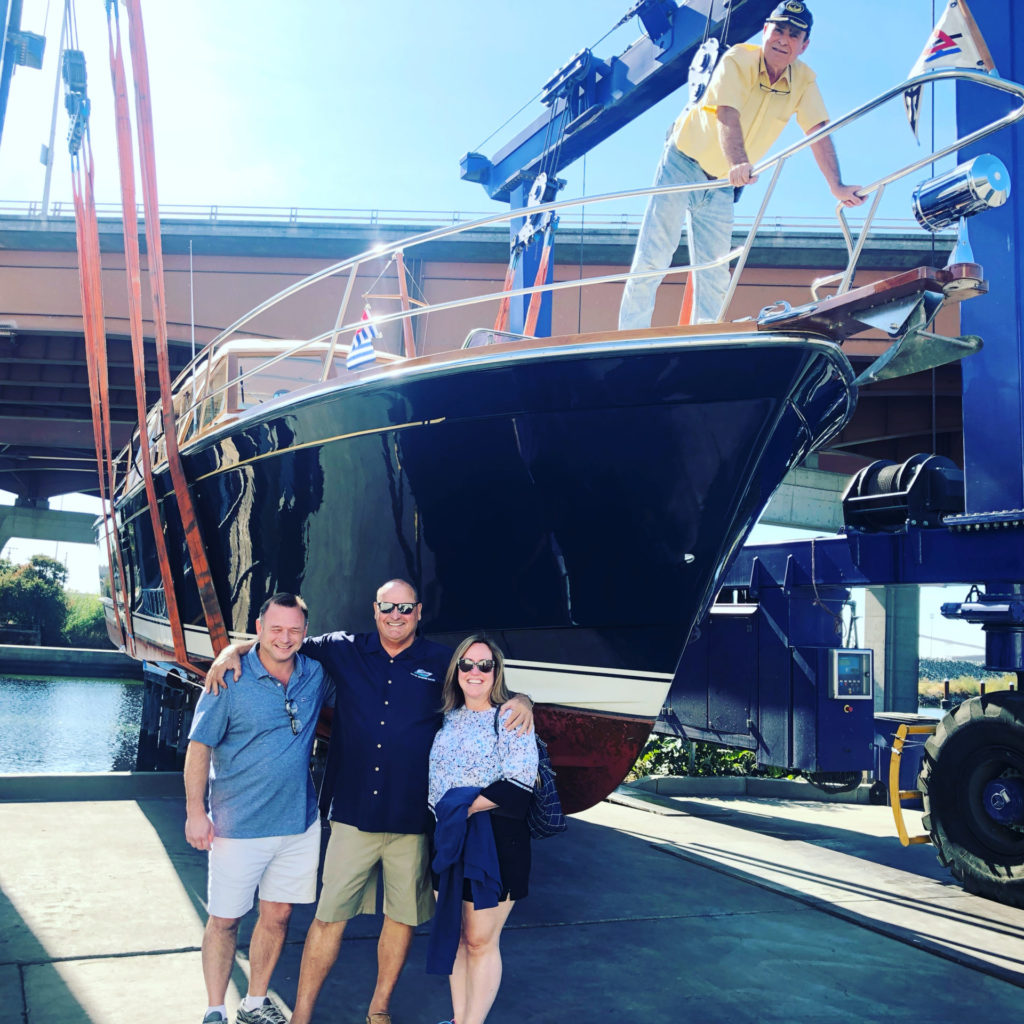 A photo of a group of people standing in front of a yacht in the boat yard at Delta Marine Sales